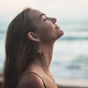Woman with long hair and earrings looking up towards the sky with a blurred natural background