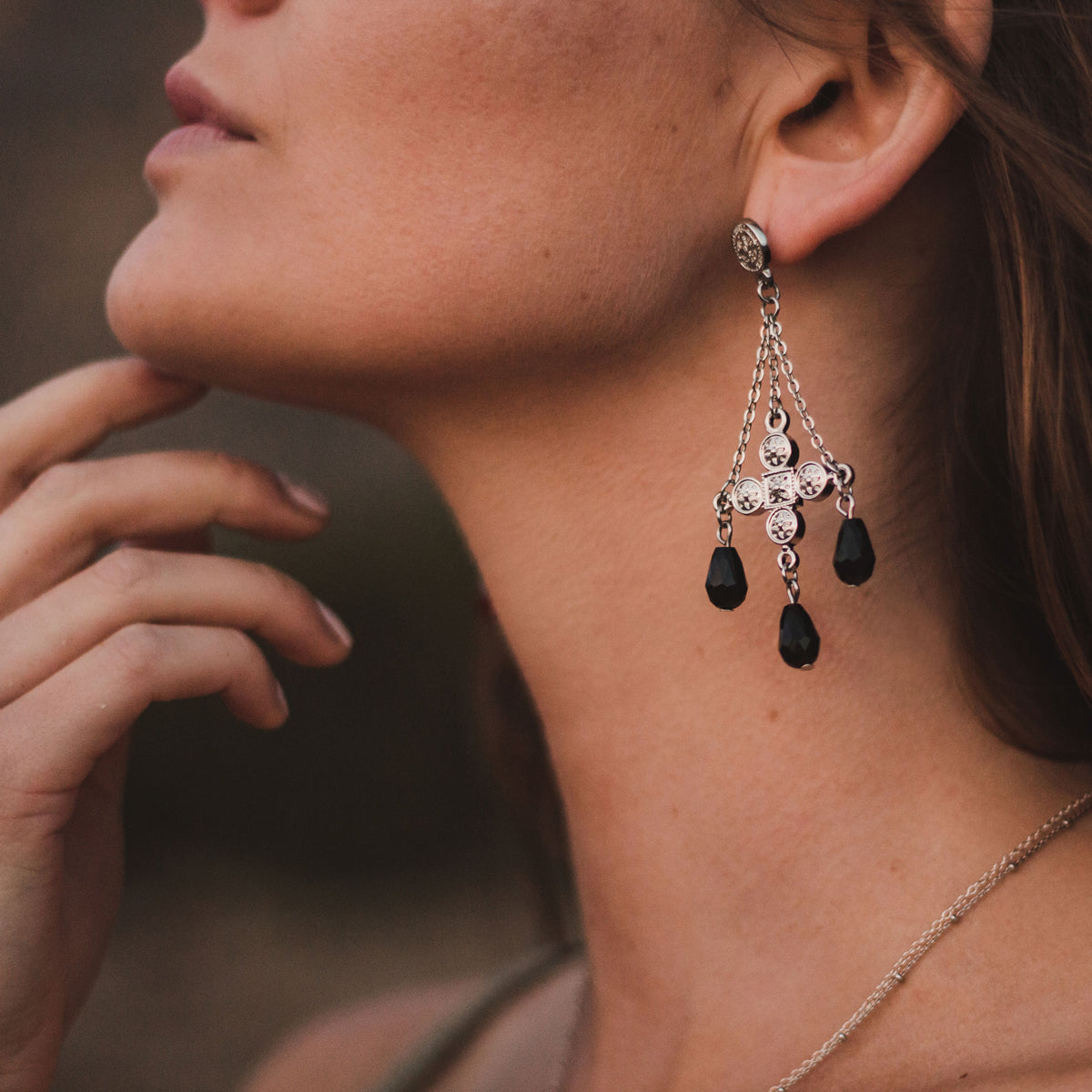 Close-up of a woman wearing Deep Faith  dangling earring with black crystals.