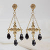 Pair of gold earrings with black teardrop charms on a light background