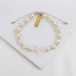 Pearl bracelet with gold accents and a cross charm on a white background