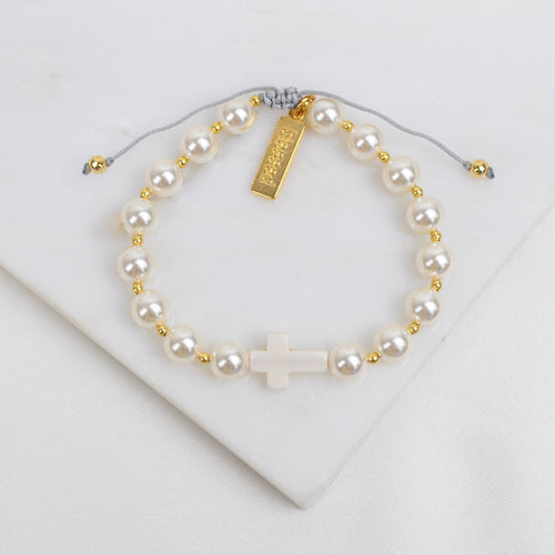 Pearl bracelet with gold accents and a cross charm on a white background