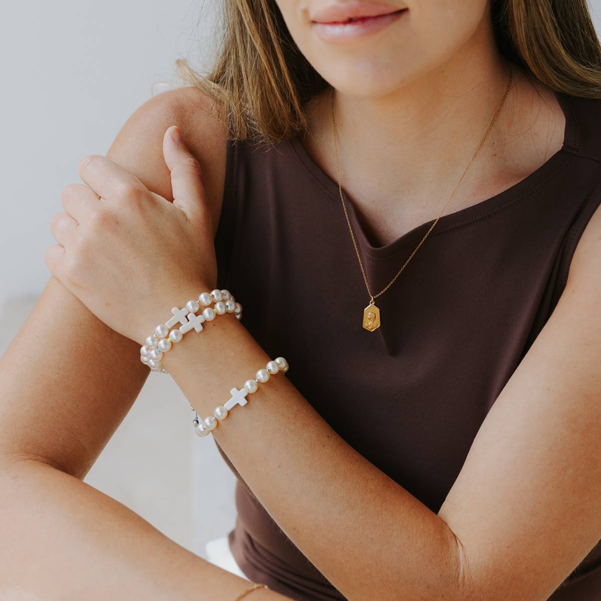 Woman wearing pearl bracelets and a gold necklace against a neutral background