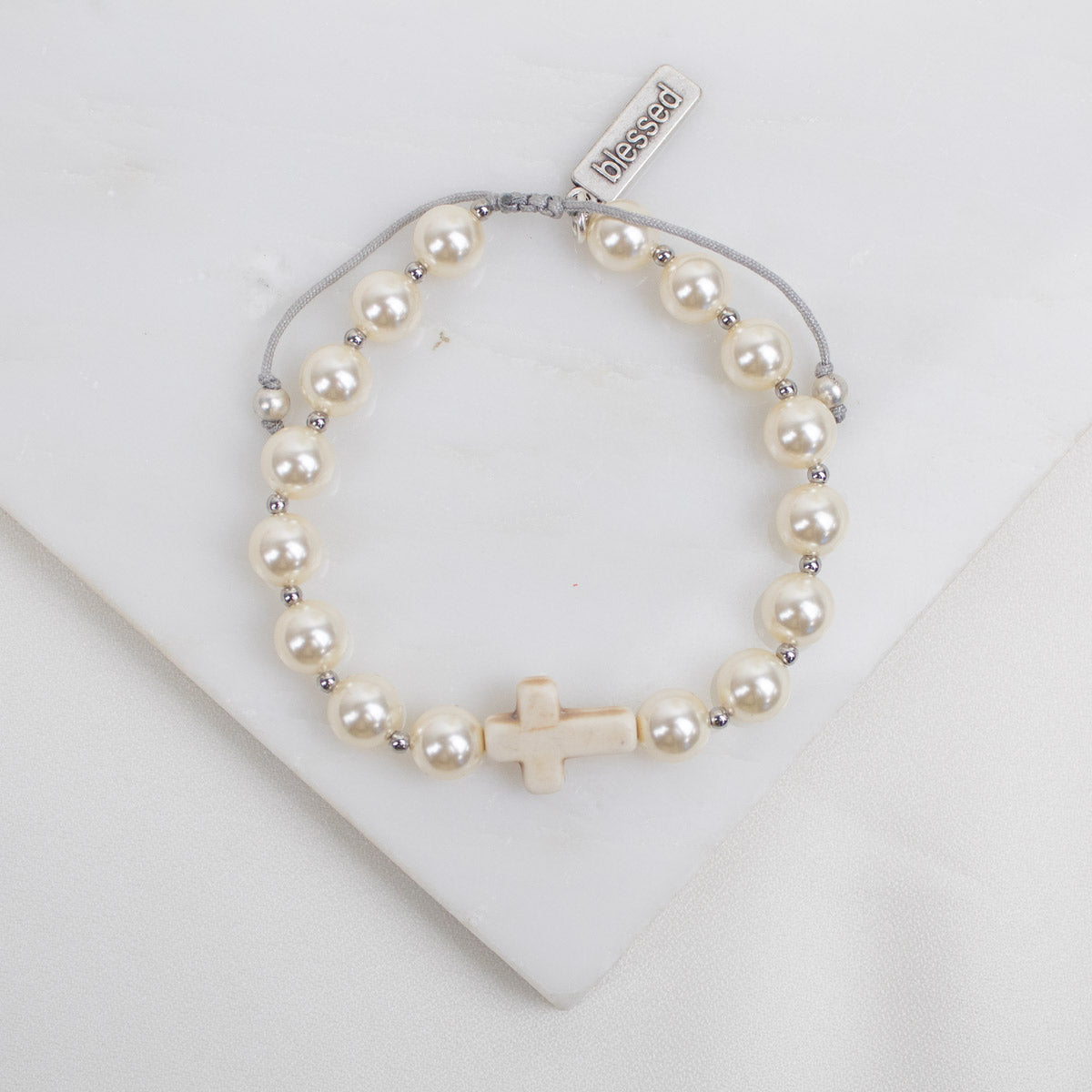 Pearl bracelet with a cross charm on a white background