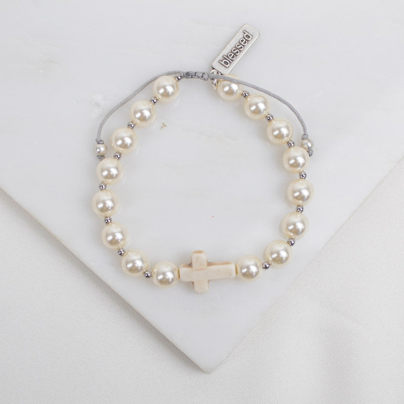 Pearl bracelet with a cross charm on a white background