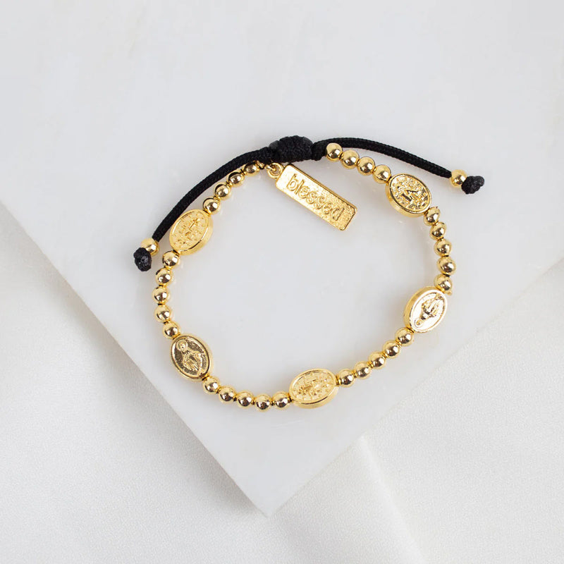 Held by Mary Gold Beads and Miraculous Mary Medal bracelet on black woven cording
