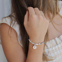 Close-up of a person wearing a bracelet with a Holy Spirit Saint Charm charm on a neutral background