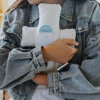 Person holding a white plush cross Huggable Prayer pillow wearing a denim jacket.