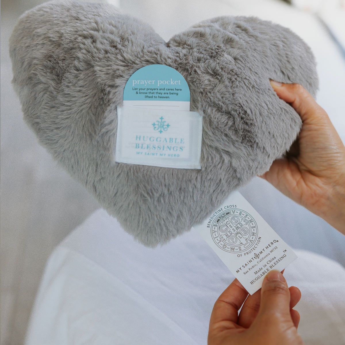 Heart-shaped plush pillow with a prayer pocket held by a hand against a white background