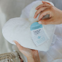 White prayer pillow with a label held by hands against a neutral background