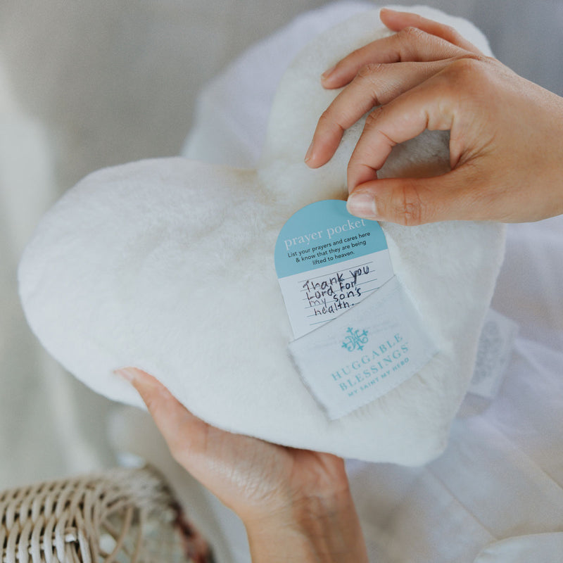 White prayer pillow with a label held by hands against a neutral background