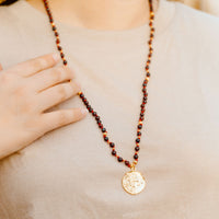 Necklace with a gold pendant worn by a person, with a hand resting on the chest.
