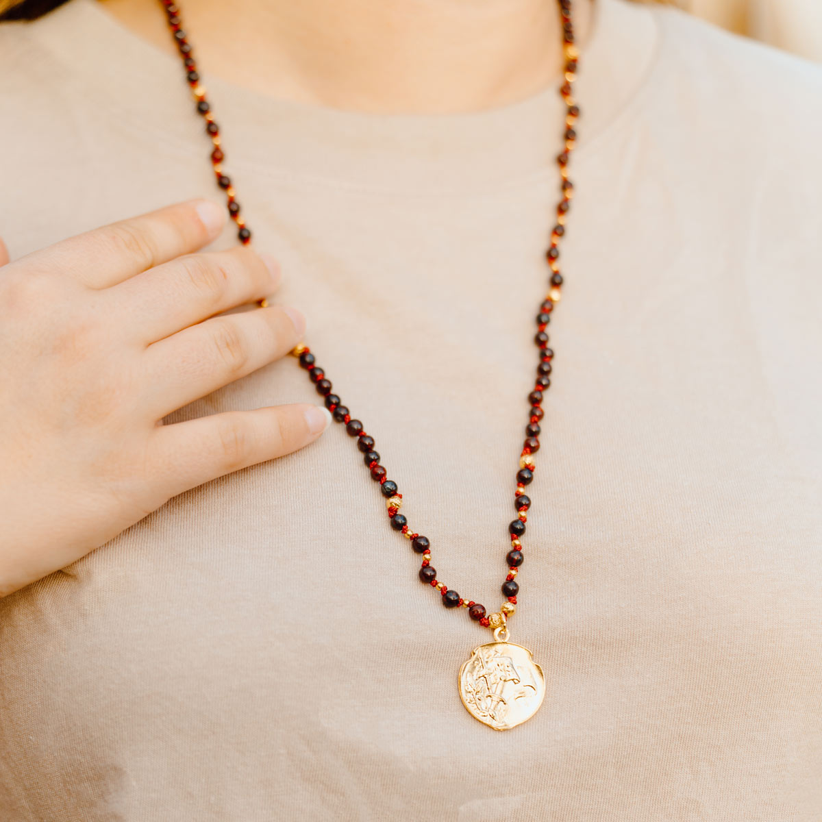 Necklace with a gold pendant worn by a person, with a hand resting on the chest.