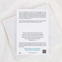 A white rectangular card with printed prayer text and branding for Wearable Blessings, placed on a light marble surface.