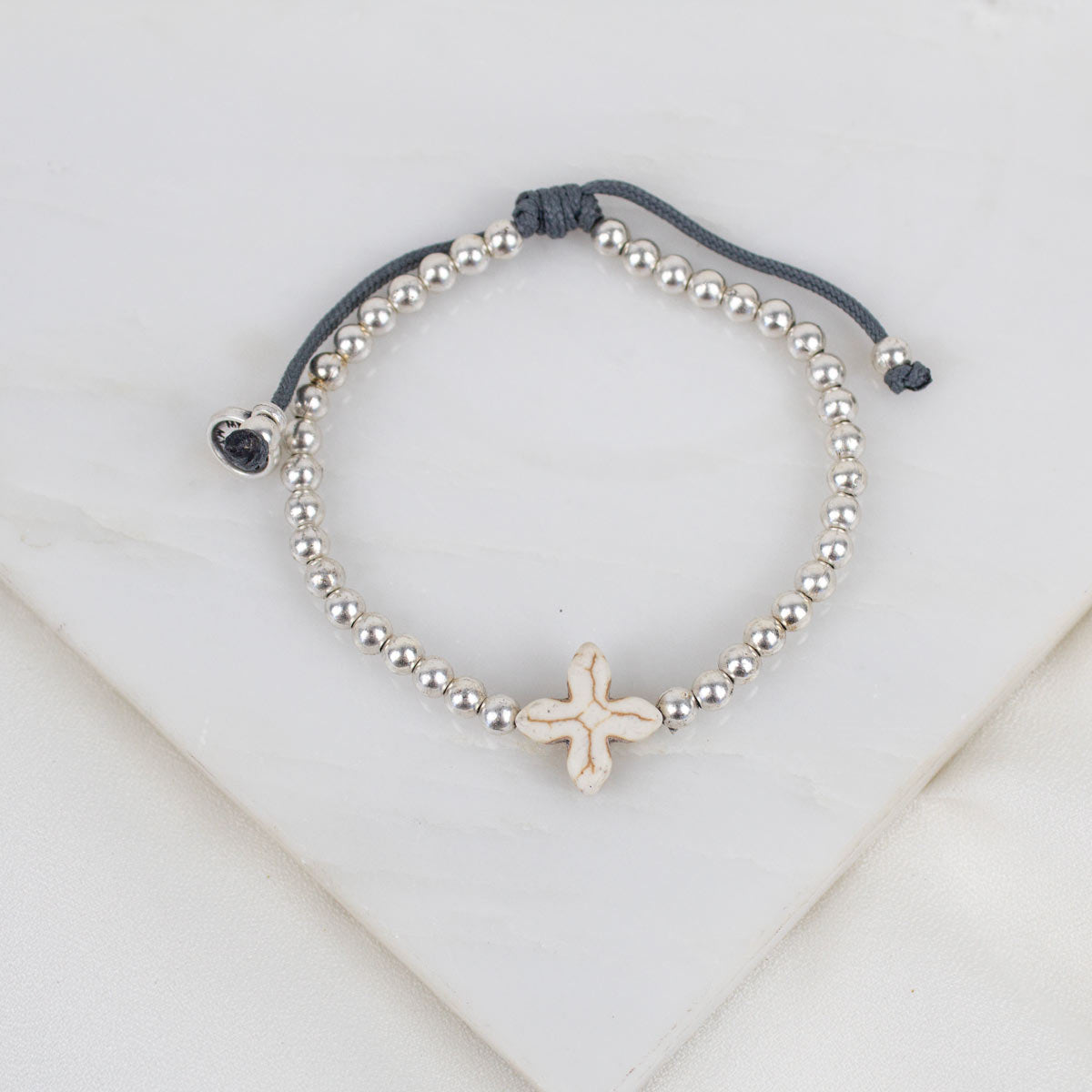 A beaded slipknot bracelet featuring a central textured howlite cross silver-toned beads, a dark gray adjustable cord.