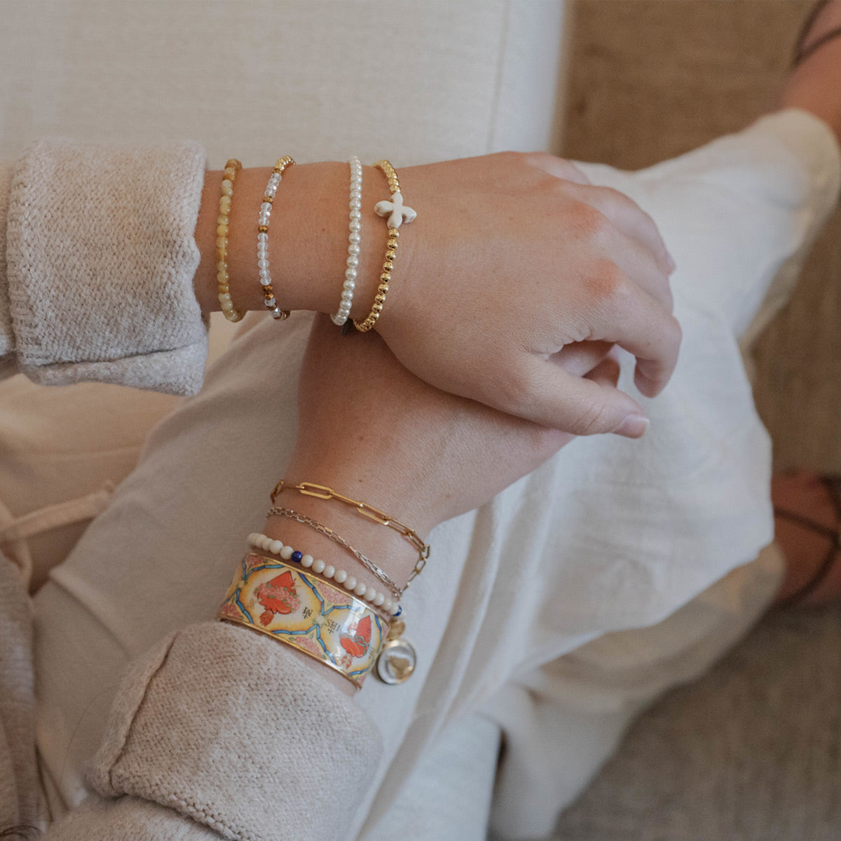 A close-up of a person's hands and wrists wearing multiple delicate bracelets, including Shine Bright, Jesus Prayer Bracelets, Let God Prayer Bracelets, Lourdes Bracelet, Healed by Faith Bracelet and a Holy Family Cuff