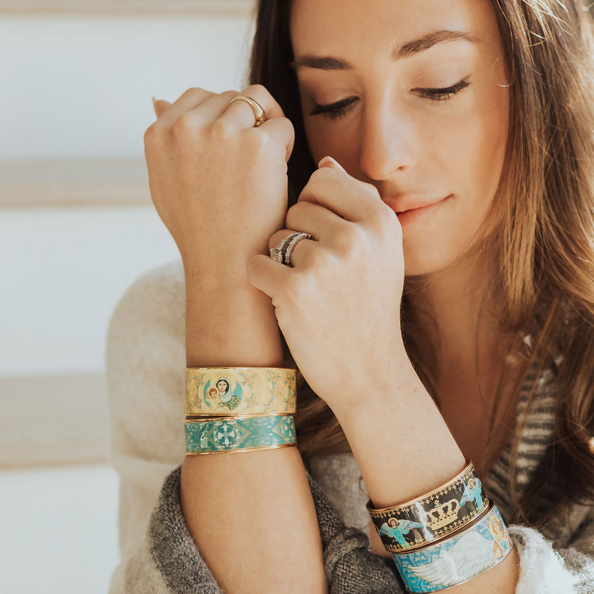 Woman wearing the My Saint My Hero Magnificat Sacred Icon gold-tone cuff bracelet stacked with colorful religious icon cuffs.