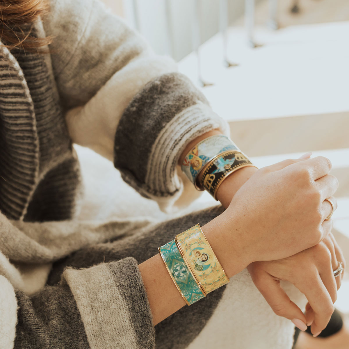 Woman wearing the My Saint My Hero Magnificat Sacred Icon gold-tone cuff bracelet stacked with colorful religious icon cuffs.