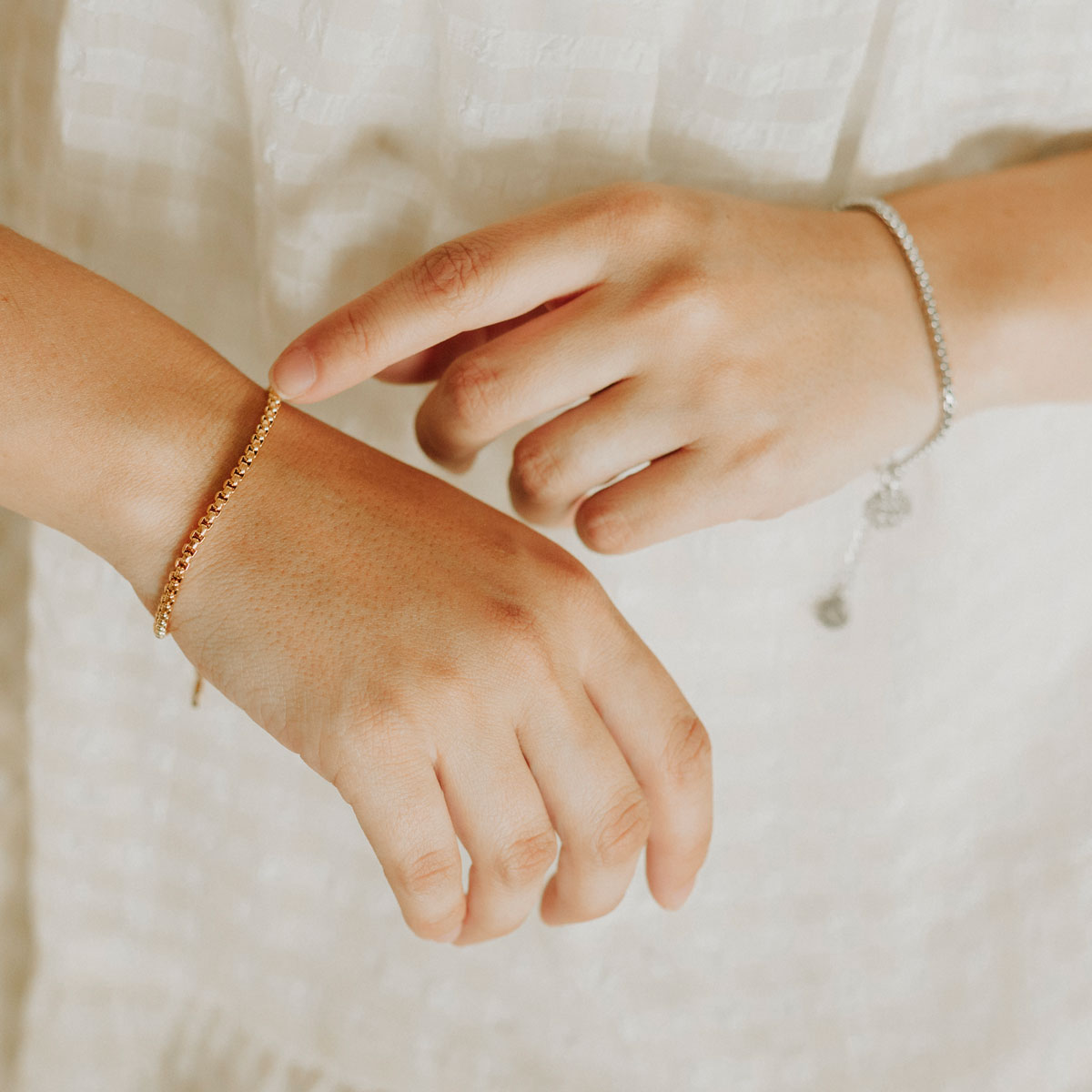 Close up of woman's hands wearing a gold and a silver consecration bracelet