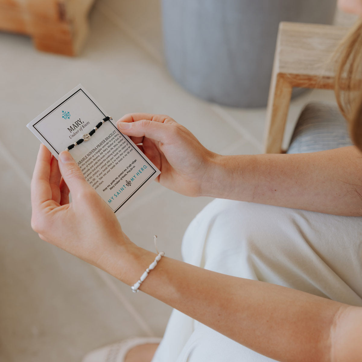 Person holding a card with a bracelet design and text, sitting on a couch.