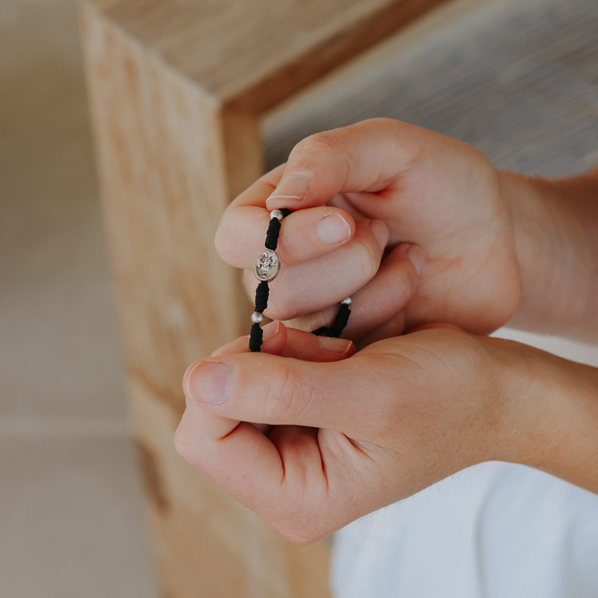 Close-up of hands holding and praying on a black Mary Undoer of Knots bracelet .