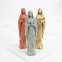 Three Our Lady of Lourdes  figurines in different colors on a white background