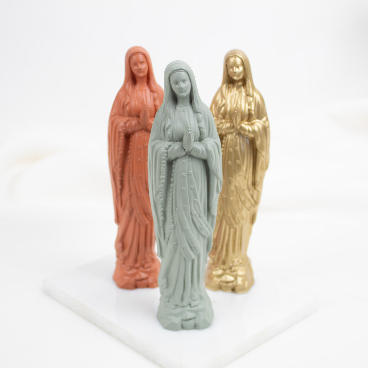 Three Our Lady of Lourdes  figurines in different colors on a white background