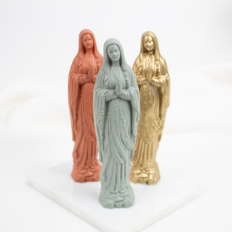 Three Our Lady of Lourdes  figurines in different colors on a white background