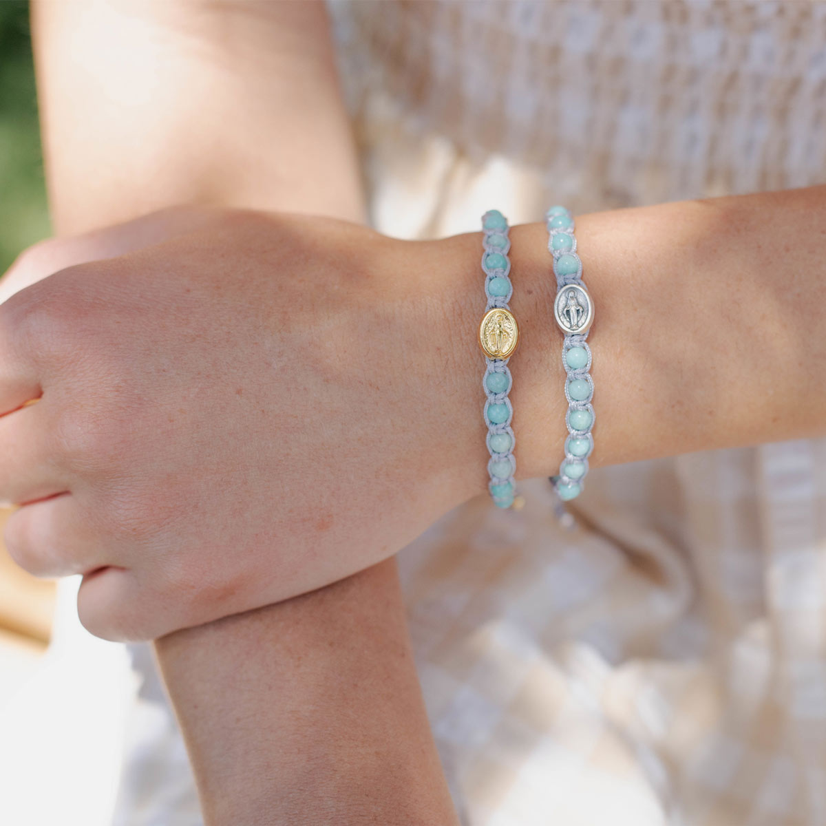 Close-up of a person's wrist wearing two light blue beaded bracelets with metal charms.