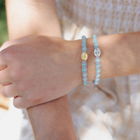 Close-up of a person's wrist wearing two light blue beaded bracelets with metal charms.