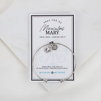Bangle with charms on a card featuring text about Miraculous Mary, on a white background.
