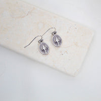Silver Miraculous Medal earrings on a marble surface