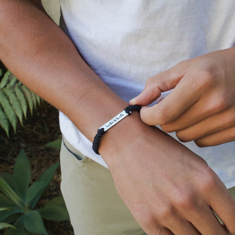 close up of man's wrist wearing a Nada Te Turbe handwoven bracelet in black cording and silver bar 