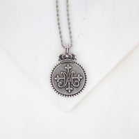 Silver necklace with a decorative Auspice Maria design pendant on a white background
