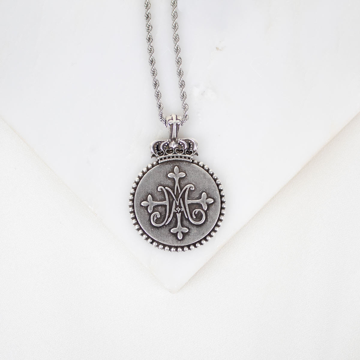 Silver necklace with a decorative Auspice Maria design pendant on a white background