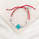 Bracelet with white beads, turquoise howlite cross bead and red string on a light background