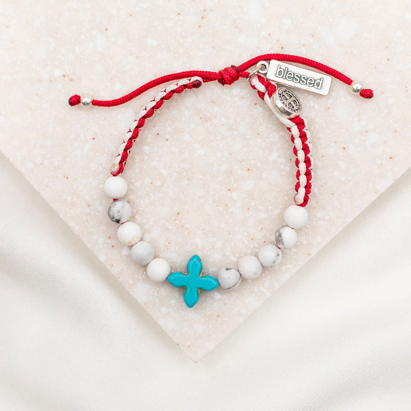 Bracelet with white beads, turquoise howlite cross bead and red string on a light background