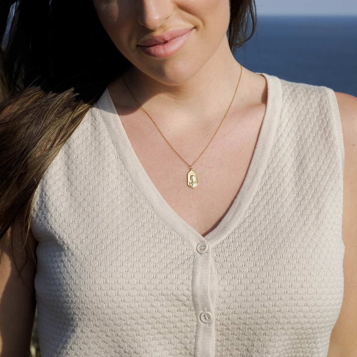 Woman with a Our Lady of Fatima gold plated necklace, wearing a beige sleeveless top with a necklace against a blurred natural background