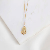 Gold necklace with a Our Lady of Fatima gold plated pendant (back of medal with the three children saints show) on a white marble surface