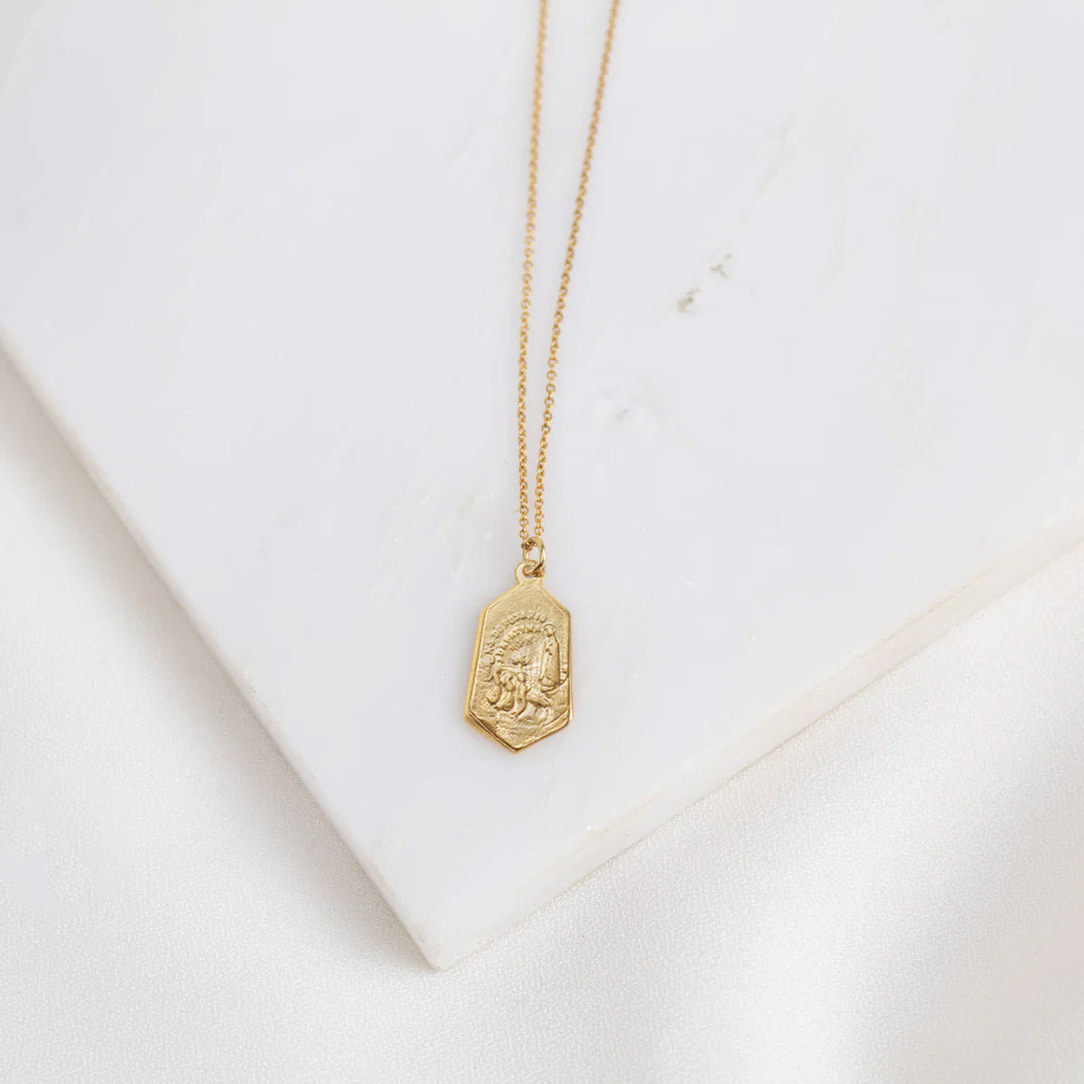 Gold necklace with a Our Lady of Fatima gold plated pendant (back of medal with the three children saints show) on a white marble surface