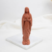 Terracotta-colored statue of Our Lady of Lourdes  on a white base