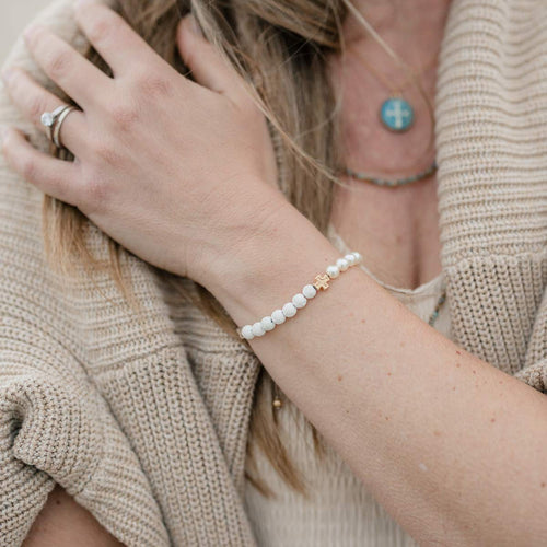 close up of woman's arm wearing Heirloom crystal pearls and white lava beads and gold cross bracelet