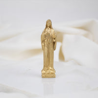 A gold-colored statue of the Virgin Mary with a floral pattern on its base, placed on a white surface.