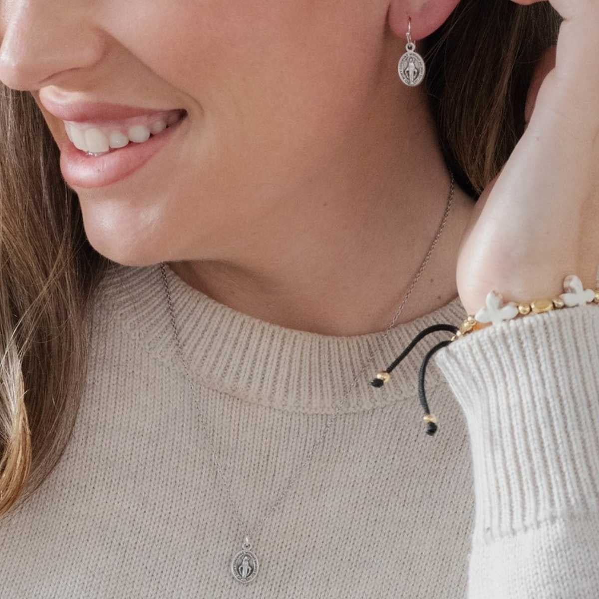 Close-up of a woman wearing silver earrings and a ring, with a neutral background.
