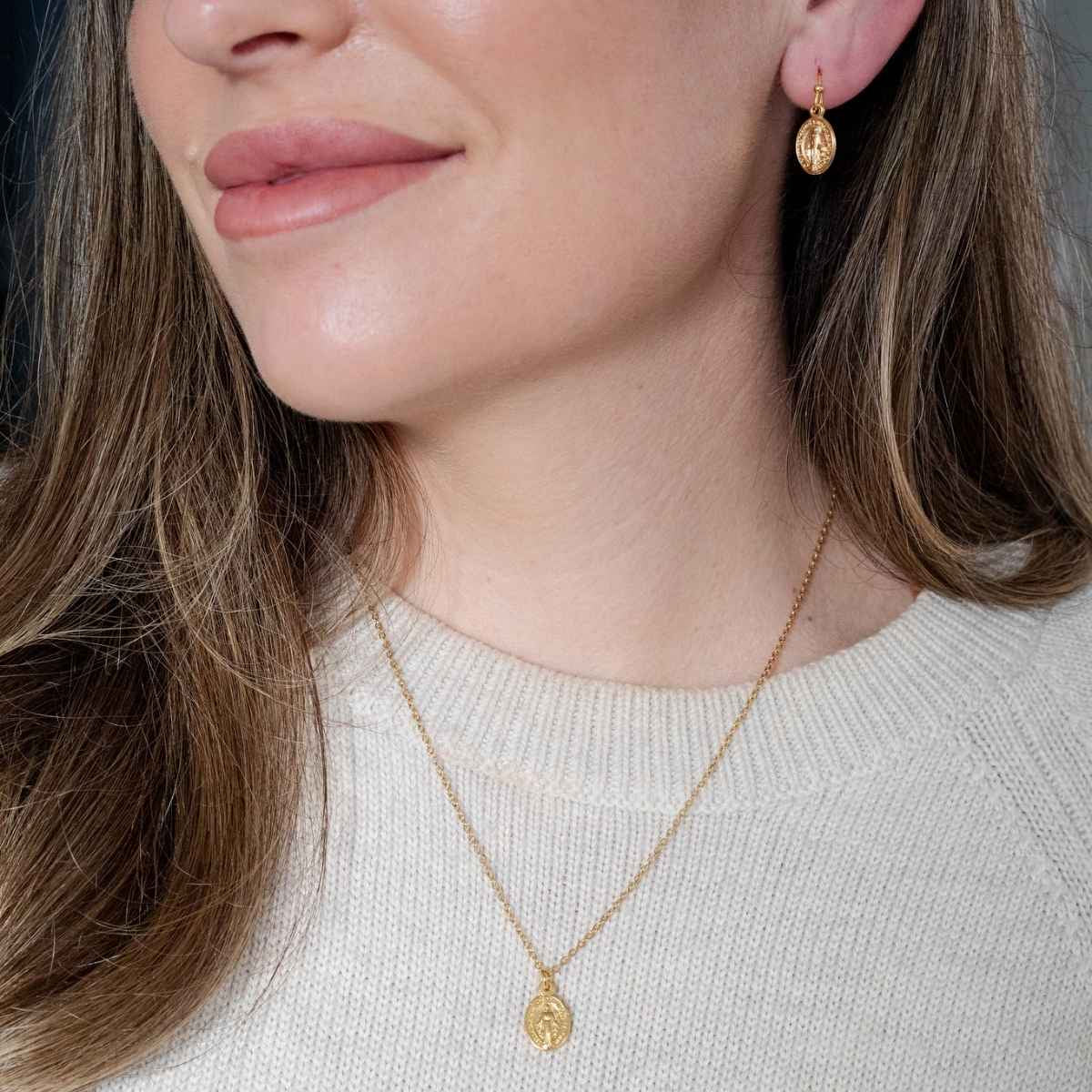 Close-up of a woman wearing gold earrings and necklace with a neutral background
