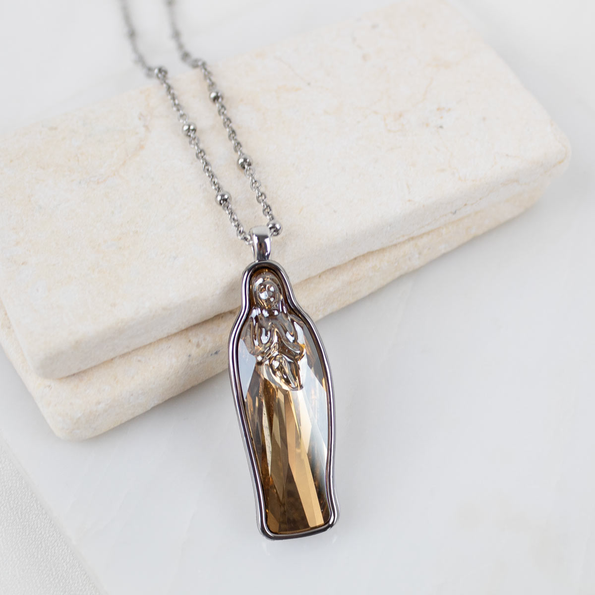 Silver chain with a gold crystal Mary pendant necklace on a white background