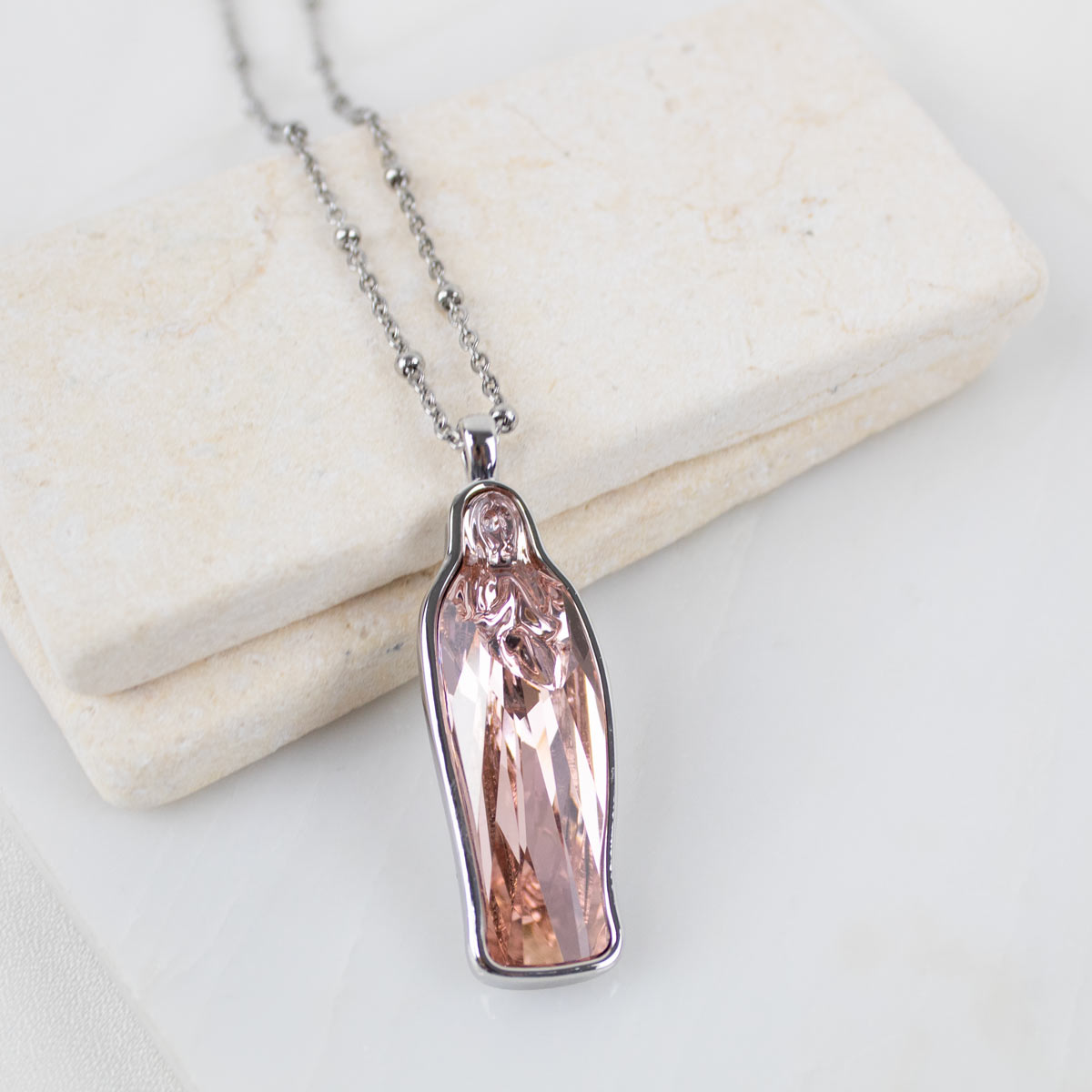 Silver chain with a pink crystal Mary pendant necklace on a light background