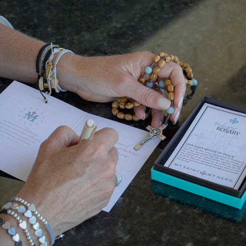 woman filling out the novena gifting card while holding the wooden and amazonite rosary