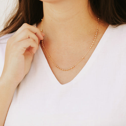 Rosary Bead Necklace in gold tone on woman in white top