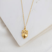 A gold-colored necklace with a heart-shaped pendant featuring a flower design, displayed against a white background.