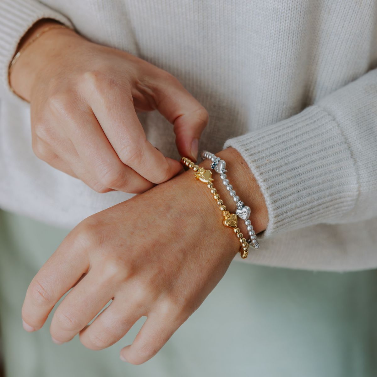 Person wearing multiple Sacred Heart bracelets on a blurred background